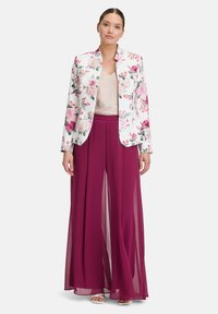 Marynarka w kwiatowy wzór w bieli z różowymi i zielonymi akcentami, zestawiona z lśniącą beżową bluzką i długimi burgundowymi spodniami z szyfonu.