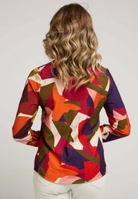 Chemise à manches longues avec un motif abstrait coloré en rouge, orange, rose, vert et violet, faite de tissu texturé, vue de dos.
