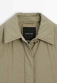 Khaki-Leichtjacke mit spitzem Kragen, Frontverschluss und einem schwarzen Etikett mit der Aufschrift "Massimo Dutti". Glatte Textur, minimalistisches Design.
