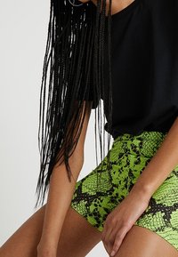 Camiseta negra de manga corta combinada con pantalones cortos verdes de talle alto con estampado de serpiente, con una superficie texturizada y un diseño ajustado.