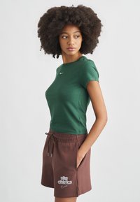 Πράσινο κοντομάνικο t-shirt από απαλό ύφασμα, με μικρό λευκό λογότυπο Nike. Συνδυασμένο με καφέ σορτς με κορδόνι, που φέρει λευκές λεπτομέρειες κειμένου και λογότυπου.