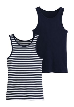 Jeune femme aux cheveux bouclés portant un haut sans manches bleu marine et blanc rayé et un jean bleu, regardant sur le côté, tenant l'ourlet de sa chemise.