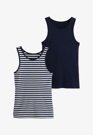 Jeune femme aux cheveux bouclés portant un haut sans manches bleu marine et blanc rayé et un jean bleu, regardant sur le côté, tenant l'ourlet de sa chemise.