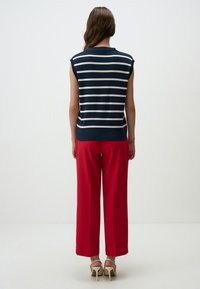 Marineblauwe en witte gestreepte mouwloze top gecombineerd met rode wijde broeken, aangevuld met beige hoge hakken en een gladde textuur.