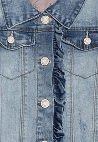 Světle modrá džínová bunda s volánovým předním dílem, stříbrnými knoflíky a kapsami na prsou. Prošlapaná textura s klasickým designem límce.