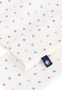 Katoenen stof met een crèmekleurige achtergrond en kleine, verspreide hartjes in roze, paars en blauw. Inclusief een blauw label aan de rand.