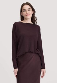 Pullover bordeaux con maniche lunghe e scollo ampio, abbinato a una gonna coordinata di lunghezza al ginocchio, realizzata in un tessuto liscio con texture minima.