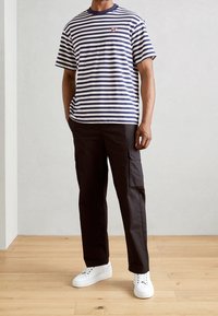 Marineblå og hvide stribede bomulds-T-shirt med rund hals, parret med sorte cargo-bukser og hvide sneakers. Synlig logo-detail på venstre bryst.