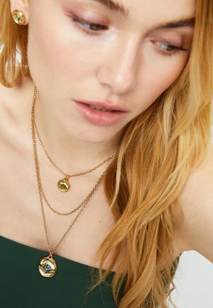 Collar en capas de tono dorado con colgantes circulares que incluyen una gema azul, que presenta un diseño de cadena elegante y superficies lisas y pulidas.