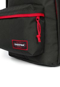 Mochila negra con acentos rojos, con una tela texturizada, bolsillo frontal con cremallera y un prominente parche con el logo de Eastpak.