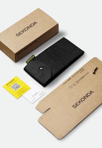 Pochette de montre en feutre noir avec fermeture à pression, placée à côté d'une boîte en carton marron imprimée "SEKONDA" et d'une carte de garantie jaune.