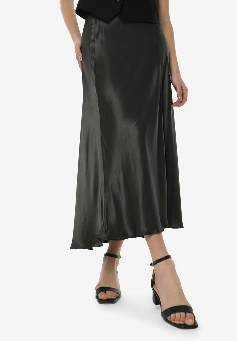 Falda midi de satén verde oscuro con un diseño fluido, abertura lateral y textura suave, combinada con sandalias negras de tiras.