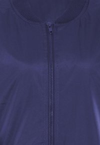 Giacca leggera blu navy con chiusura a zip, colletto a coste e texture liscia, progettata con un'estetica minimalista.