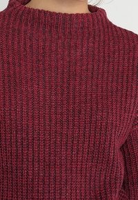 Maglione rosso a coste con collo alto, caratterizzato da un tessuto mixato testurizzato e una vestibilità ampia e rilassata.
