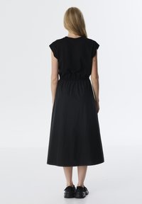 Abito nero con un top aderente e una vita elasticizzata, caratterizzato da una gonna fluida di lunghezza media fino al polpaccio e maniche corte. Design minimalista.