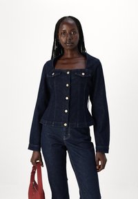 Giubbotto in denim blu scuro con scollatura quadrata, maniche lunghe, bottoni dorati e due tasche sul petto. Abbinato a pantaloni in denim coordinati.