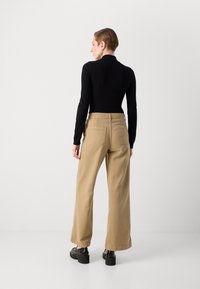 Svart langermet topp kombinert med vide khaki-bukser. Bukser har baklommer og en jevn tekstur. Sorte plattform-sko fullfører antrekket.