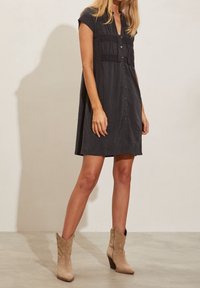 Kolgrå skjortklänning med korta ärmar, texturerade frontpaneler och A-linjeform. Bärs med beige klackade ankelstövlar.