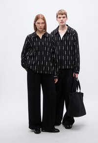 Μαύρα πουκάμισα με μακριά μανίκια και λευκές κάθετες γραμμές· φαρδιά μαύρα παντελόνια· μαύρη τσάντα ώμου· λεία υφή· μινιμαλιστικός σχεδιασμός.