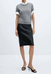 Grau gestrickter Pullover mit umgeschlagenen kurzen Ärmeln und weißem Kragen, kombiniert mit einem taillierten schwarzen Lederrock und schwarzen offenen Schuhen mit Absatz.