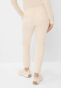 Beige corduroy broek met een slim fit en een elastische tailleband, voorzien van twee achterzakken en een cropped lengte, gecombineerd met beige sneakers.