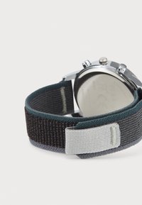 Orologio con cassa in metallo argentato, cinturino in tessuto nero e verde acqua, e dettagli grigi. Il cinturino presenta una trama intrecciata e una chiusura regolabile.