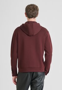 Felpa bordeaux con cappuccio, caratterizzata da una texture liscia, polsini a coste e una vestibilità morbida, abbinata a pantaloni neri di pelle.