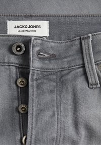 Harmaa farkkukangas, jossa on nappisulku, kontrastoiva ompelu ja etiketti, jossa lukee "JACK & JONES JEANS INTELLIGENCE."
