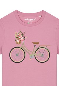 T-shirt rose avec un graphique de bicyclette. Le vélo est vert avec un siège marron et un panier rempli de fleurs roses.