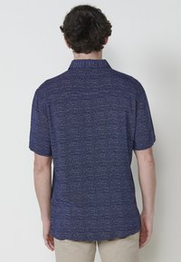 Camicetta a maniche corte di colore blu scuro con un motivo tessuto e una leggera effetto melangiato. Presenta un colletto standard e una vestibilità rilassata.