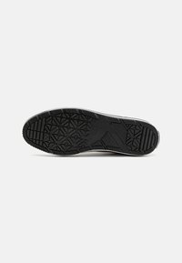 Talpa de sneaker din cauciuc negru, cu modele texturate pentru aderență și caneluri laterale, având un logo embossat la călcâi.
