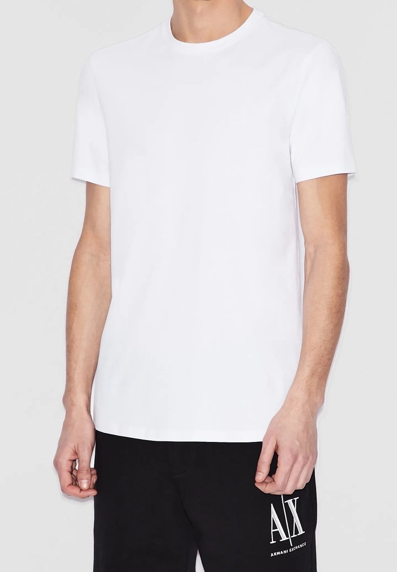 Vit T-shirt med kort ärm i bomullsmaterial, rund nacke och en subtil logotyp på bröstet, i kombination med svarta byxor med vit tryck.