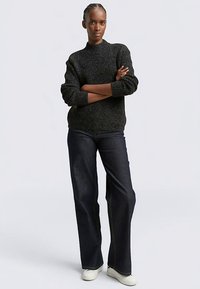 Dunkel strukturierter Strickpullover mit hohem Kragen, kombiniert mit weit geschnittenen, dunklen Jeans und weißen Sneakers mit kontrastierenden Nähten.