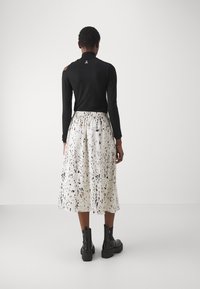 Black long-sleeve top with cutout shoulder detail and a high neckline, paired with a white midi skirt featuring a black splatter pattern.