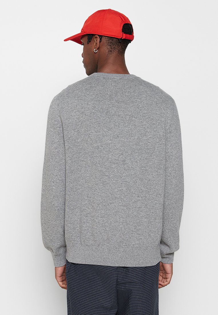 Maglione grigio a maglia con maniche lunghe, collo arrotondato e orlo a coste. Il tessuto appare morbido con una fine trama, mostrato indossato di spalle.