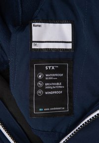 Navy blue waterproof jacket interior label displaying care instructions: STX branding, waterproof rating 10,000 mm, breathable, windproof.