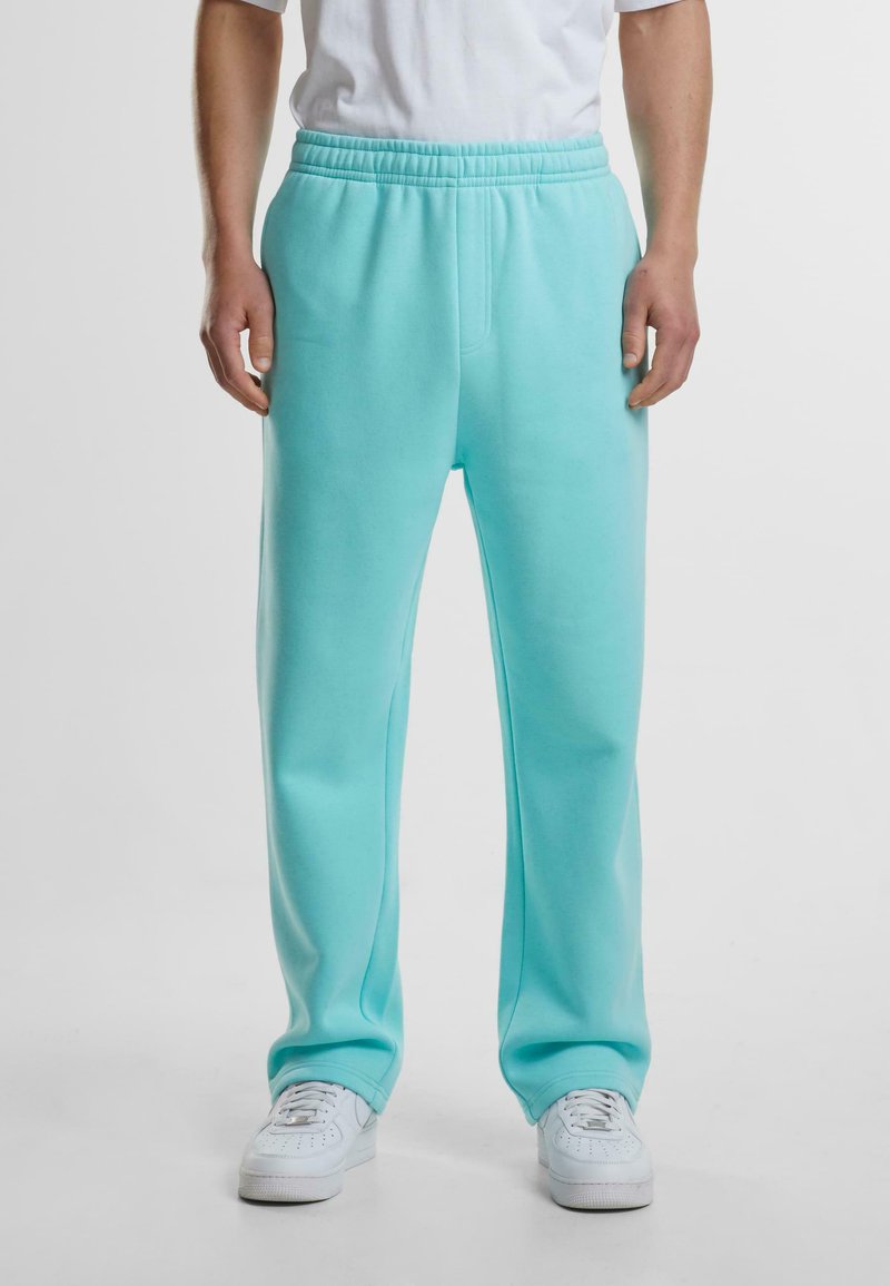 Light teal sweatpants with an elastic waistband, side pockets, and a relaxed fit. Worn with white sneakers. Soft cotton blend material.