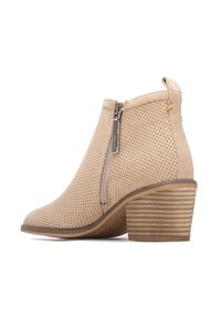 Botines beige con ante perforado, cierre lateral con cremallera y tacón apilado a rayas. Textura suave y diseño de punta redondeada.