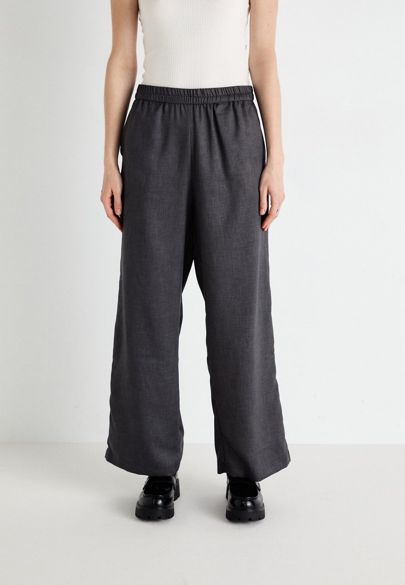 Grijze wijde broek met een elastische tailleband, gemaakt van textuurstof. Geld met zwarte schoenen, ontworpen voor comfort en gemak.