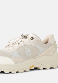 Light beige athletic shoe with mesh and suede materials, featuring a logo on the side, rubber sole, and a lacing system with a toggle.