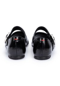 Ballerines en cuir noir avec une finition brillante, sangle arrière, éléments en argent et un petit accent rouge près du talon.