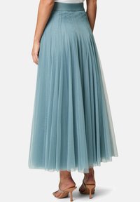 Light blue tulle maxi skirt with pleated design, elastic waistband, and a flowy silhouette, paired with beige high-heeled sandals.