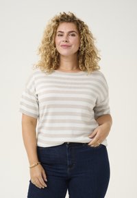 Lichtbeige gestreepte gebreide trui met korte mouwen, ronde hals en subtiele glitter, gedragen met donkerblauwe denim jeans.