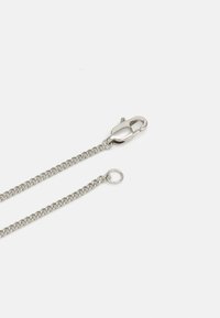 Chaîne en métal argenté avec des maillons et un fermoir. La chaîne se termine par une boucle, présentant une texture lisse et un design uniforme.