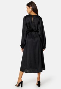 Černé saténové šaty s dlouhými nabíranými rukávy, staženým pasem a detaily ve tvaru klíčové díry na zádech. Mají volnou siluetu a volánkové akcenty na rukávech.