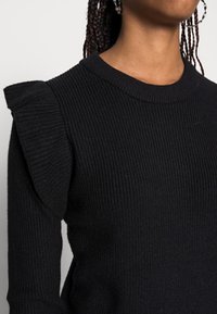 Maglione nero a costine con scollatura rotonda e dettagli arricciati sulle spalle, realizzato in un materiale di maglia testurizzato.