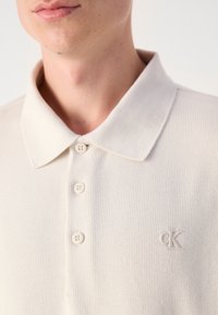 Polohemd in Hellbeige mit strukturierter Maschenware, einem flachen Kragen und drei Knöpfen. Verfügt über ein geprägtes Logo auf der linken Brust.