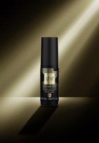 Flacon cylindrique noir de spray fixant pour boucles ghd Curly Ever After en format voyage avec étiquette dorée, mis en lumière sur un fond sombre.