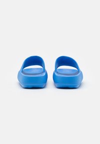 Sandali in plastica blu con suola texturizzata e retro aperto. Le cinghie sono lisce e la forma complessiva è arrotondata e minimale.