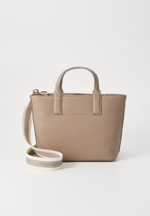 Beżowa skórzana torebka z dwoma górnymi uchwytami i odpinanym białym paskiem na ramię z marką "Tommy Hilfiger" na jednokolorowym tle.